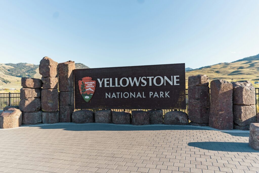 Yellowstone National Park entrance sign with stone structure and scenic mountain backdrop, highlighting Teton Expeditions' tour destinations.