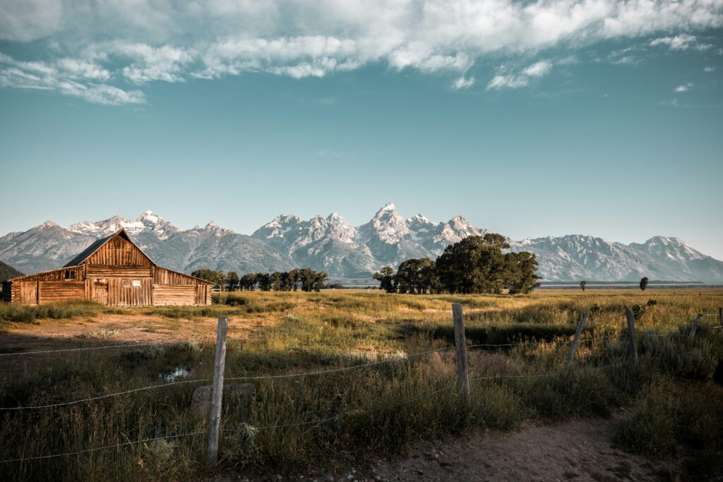 Scenic view of a rustic barn in front of the Teton mountains, highlighting the natural beauty of the Teton and Yellowstone areas.