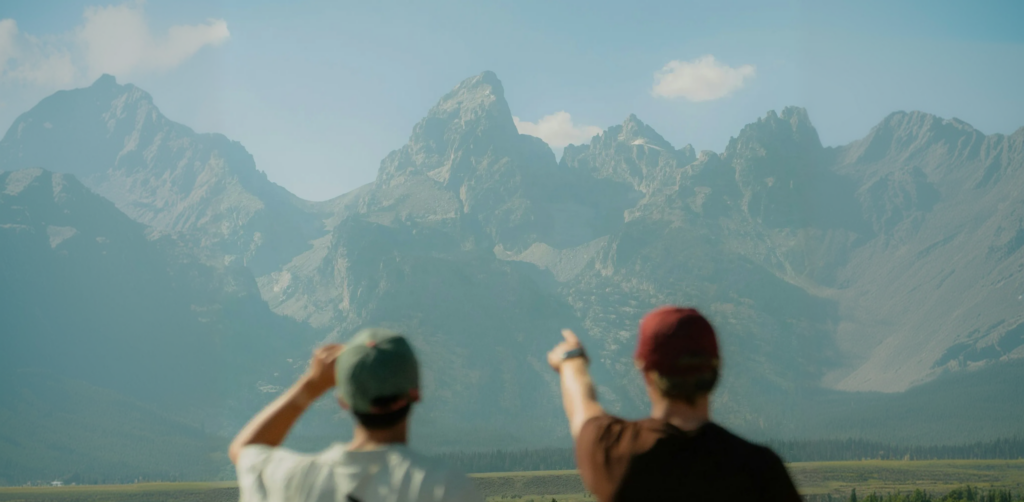 Two individuals admiring and pointing towards the majestic Teton mountain range, showcasing the stunning natural beauty of the area, relevant to Teton Expeditions' scenic tours.