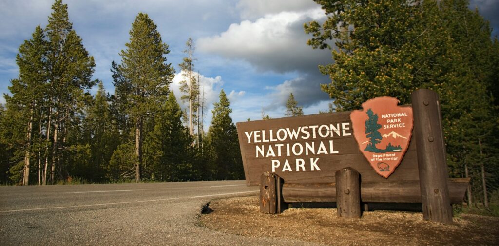 Yellowstone National Park entrance sign surrounded by lush trees, highlighting scenic beauty and adventure opportunities for Teton Expeditions tours.