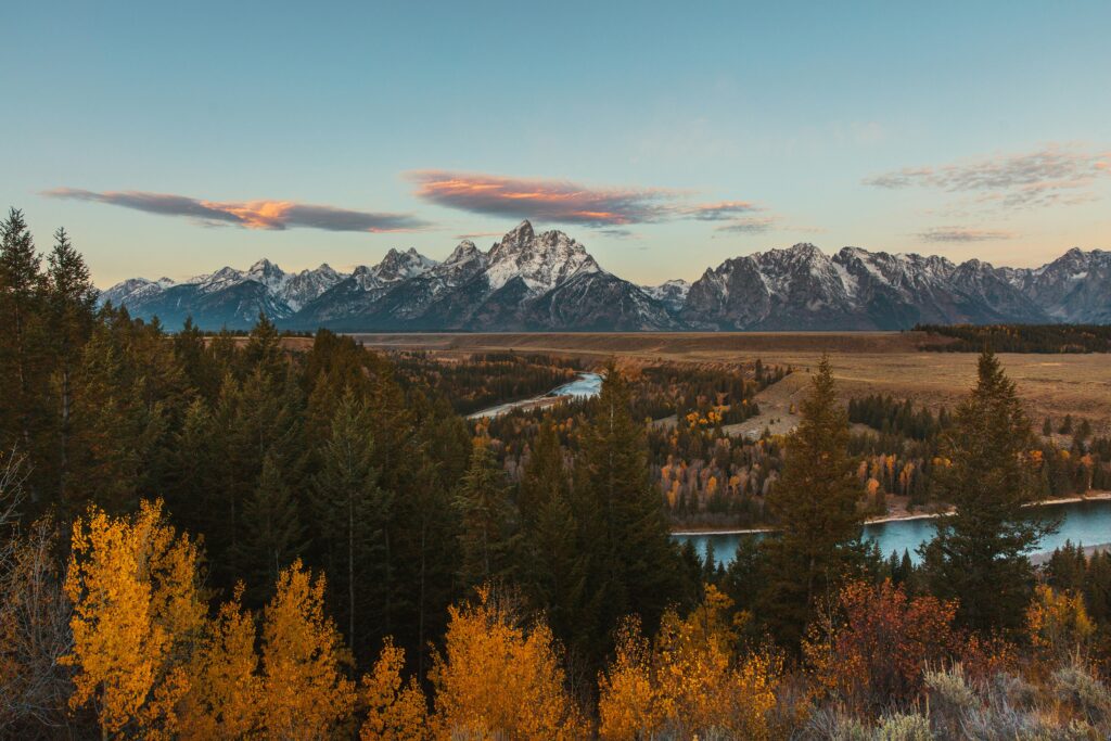 Scenic view of the Teton mountain range with autumn foliage and river, showcasing the natural beauty of Yellowstone and Grand Teton National Parks.
