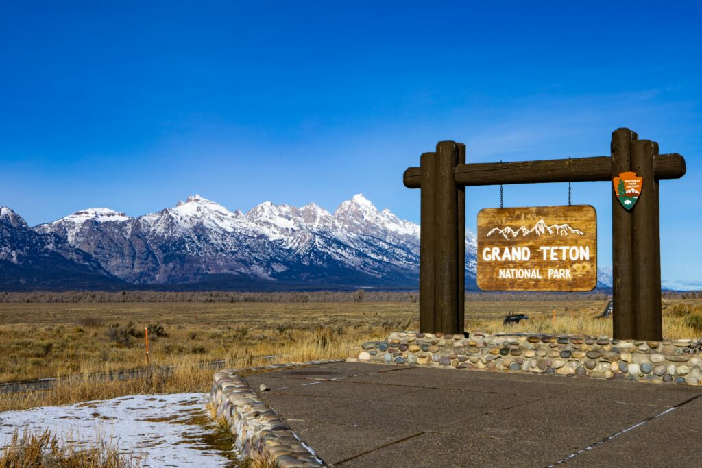 Grand Teton National Park entrance sign with snow-capped mountains in the background, highlighting scenic outdoor adventures in the Teton area.