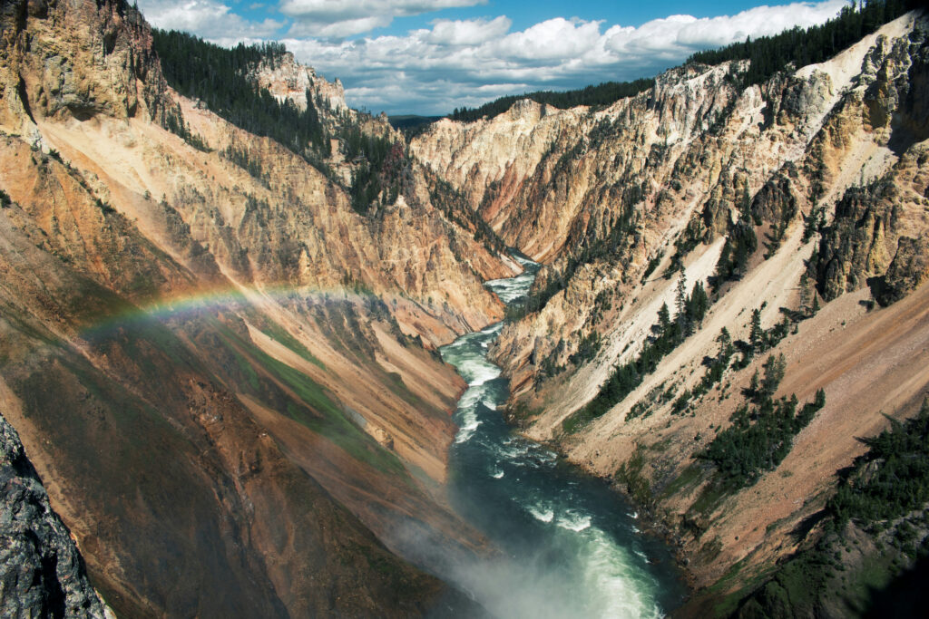Majestic view of Yellowstone Canyon with vibrant rainbow, showcasing the rugged landscape and flowing river, highlighting scenic beauty for Teton Expeditions tours.