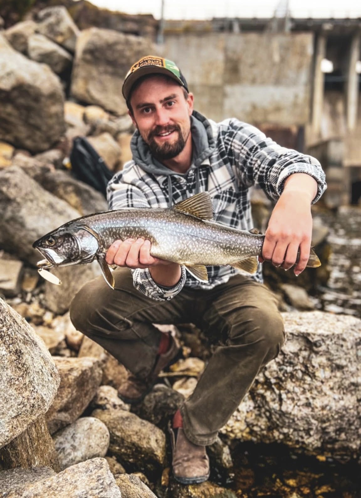 Man holding a large fish on rocky shore, showcasing outdoor adventure and fishing experiences in Wyoming, relevant to Teton Expeditions' guided tours and nature exploration.